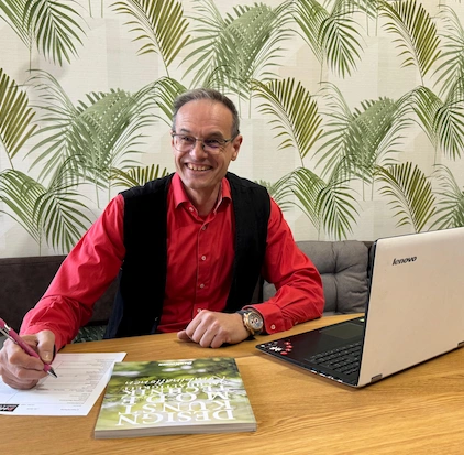 Inhaber Dietmar Haring bei der Küchenberatung und Planung am Tisch, mit Laptop, einem Katalog und einem grünen Hintergrund. 