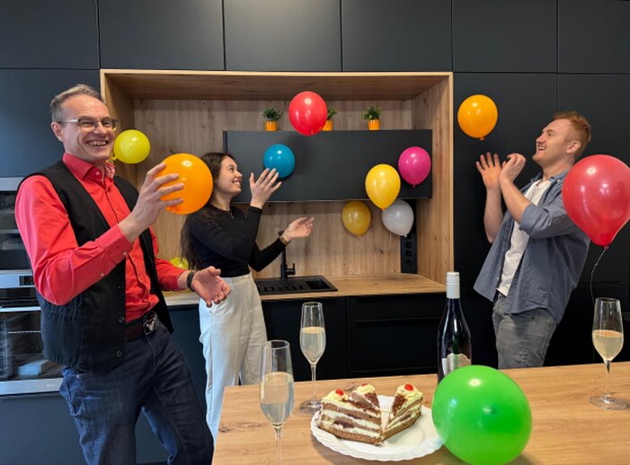 Teamfoto beim Feiern der Hausmesse 2025 mit Luftballons, Kuchen und Sekt.