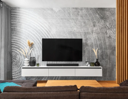 Moderne TV-Wand mit schwebendem Lowboard, grauer Wandgestaltung und Holzlamellen rechts daneben.