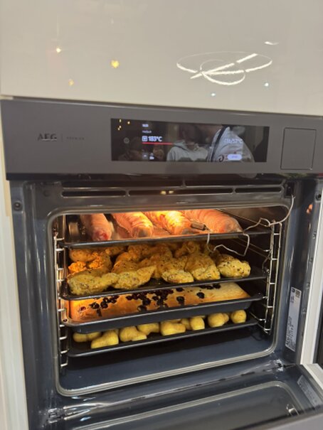 <br />Ein geöffneter AEG Dampfbackofen mit mehreren Blechen frisch zubereiteter Speisen während der Kochshow im DANKÜCHEN Küchenstudio.