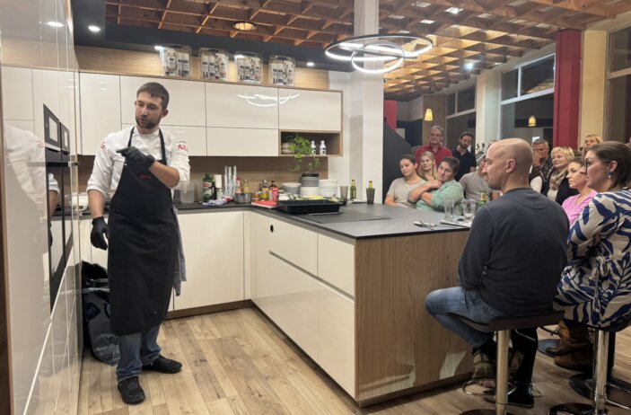 Showkoch Markus Grillenberger erklärt den Gästen die Zubereitung der Speisen während der Live-Kochshow in einer Ausstellungsküche von D.Haring in Oberndorf. Die Besucher verfolgen die Vorführung direkt an der Kochinsel.