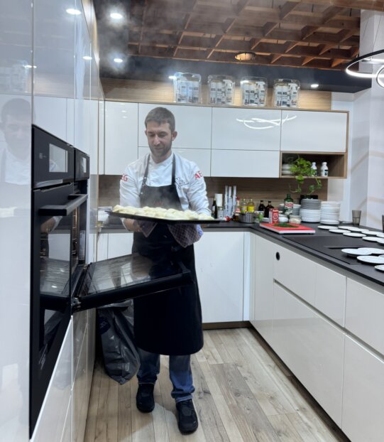 Markus Grillenberger nimmt bei der Kochshow im Studio heißes Blech aus dem AEG Dampfbackofen heraus. 