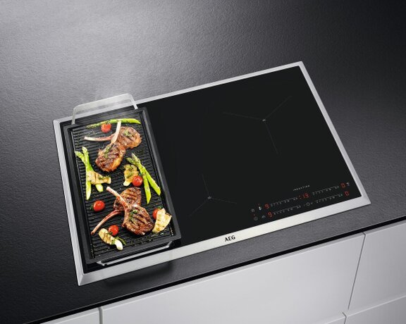 Induktionskochfeld Induktionskochfeld der Marke AEG, auf der linken Seite mit einer Grillplatte voller Gemüse.
